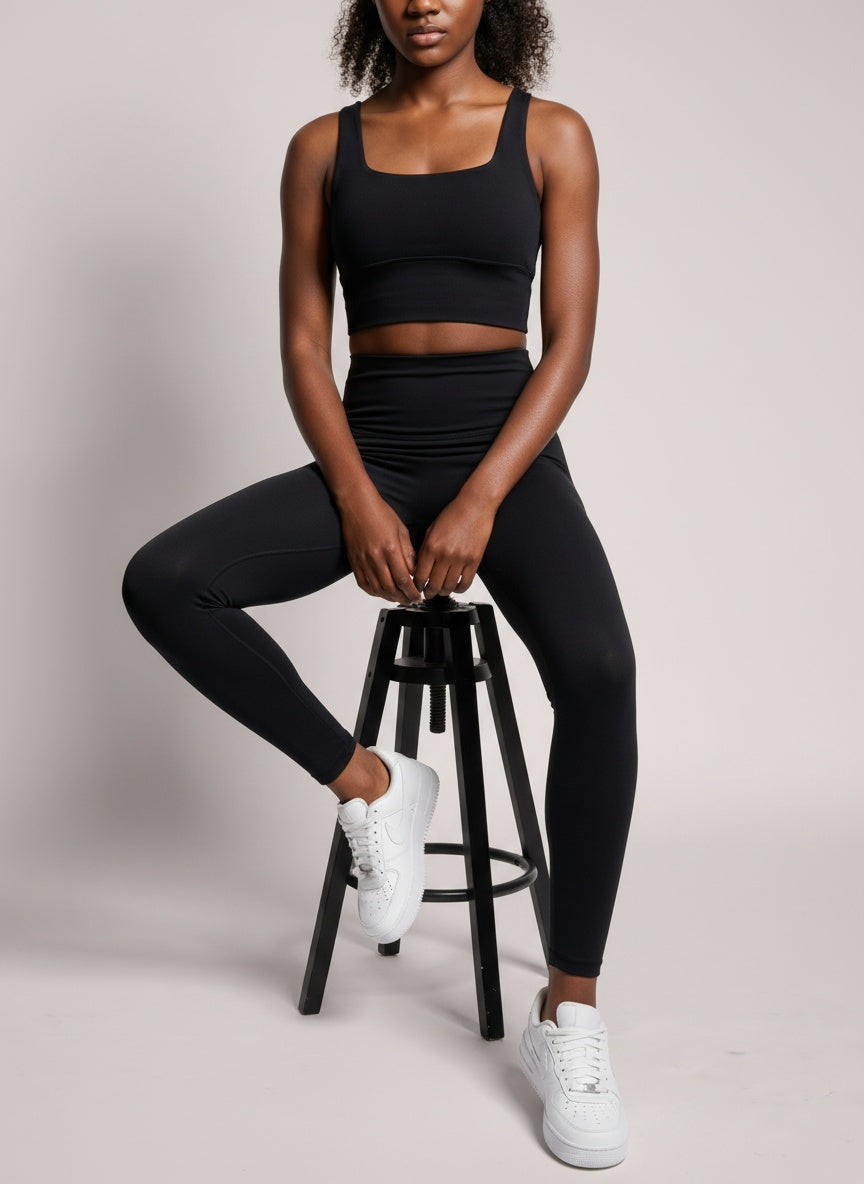Person wearing a black athletic outfit sitting on a stool against a plain background